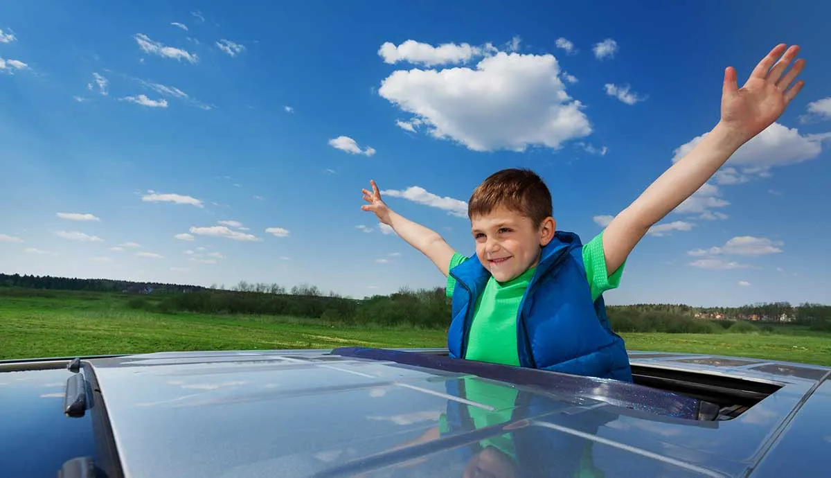 Portrait of happy smiling five years old boy enjoying freedom on the sunroof of a car